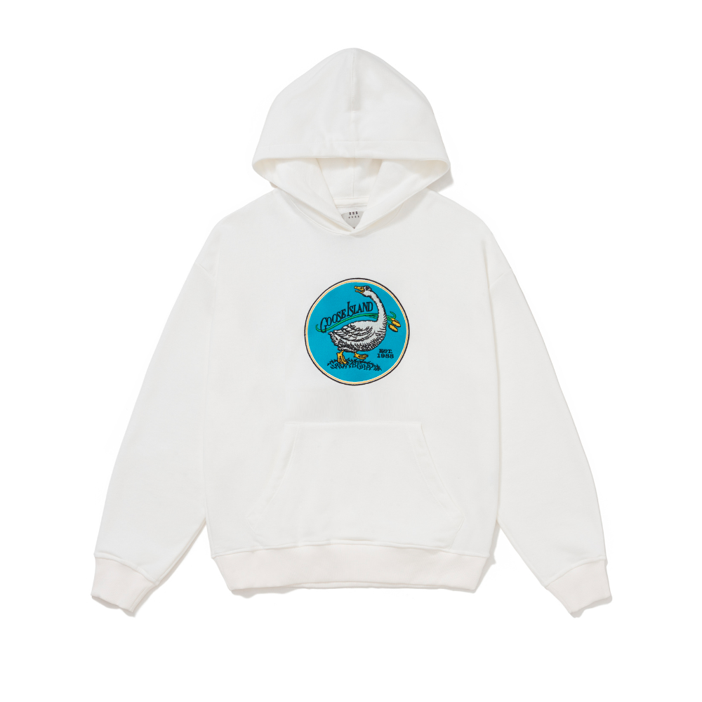 Foto Still do moletom com capuz Kiji x Goose Island Logo Retrô Off White, a estampa consiste no logo retrô da marca: um circulo azul com o desenho de um ganso ao centro, na parte superior esquerda do circulo está escrito "Goose Island" e na parte inferior direita "Est. 1988". A estampa é bordada