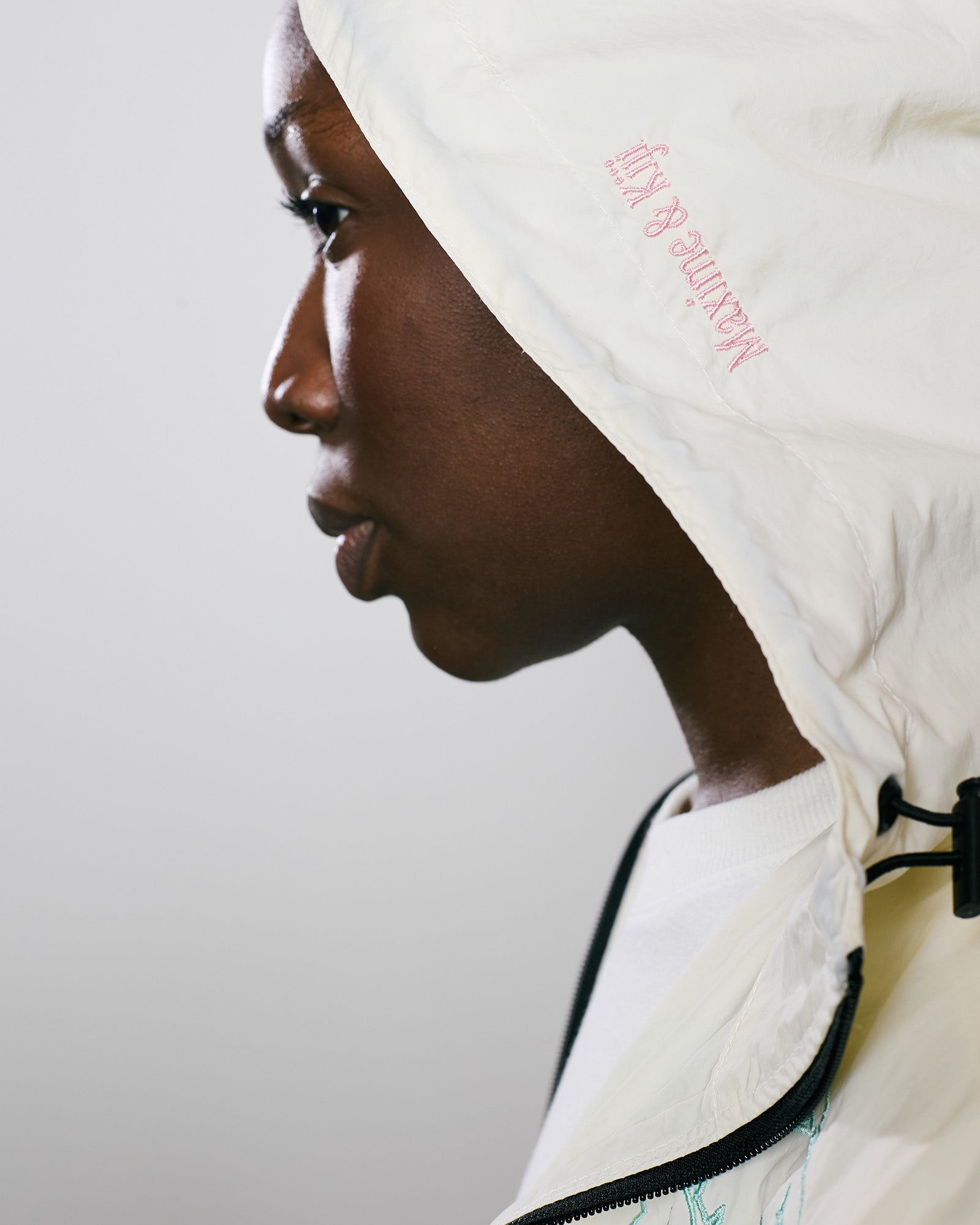 Vista lateral da Jaqueta Wind Kiji x Maxime na cor Off White, com capuz ajustável e detalhes estilosos.