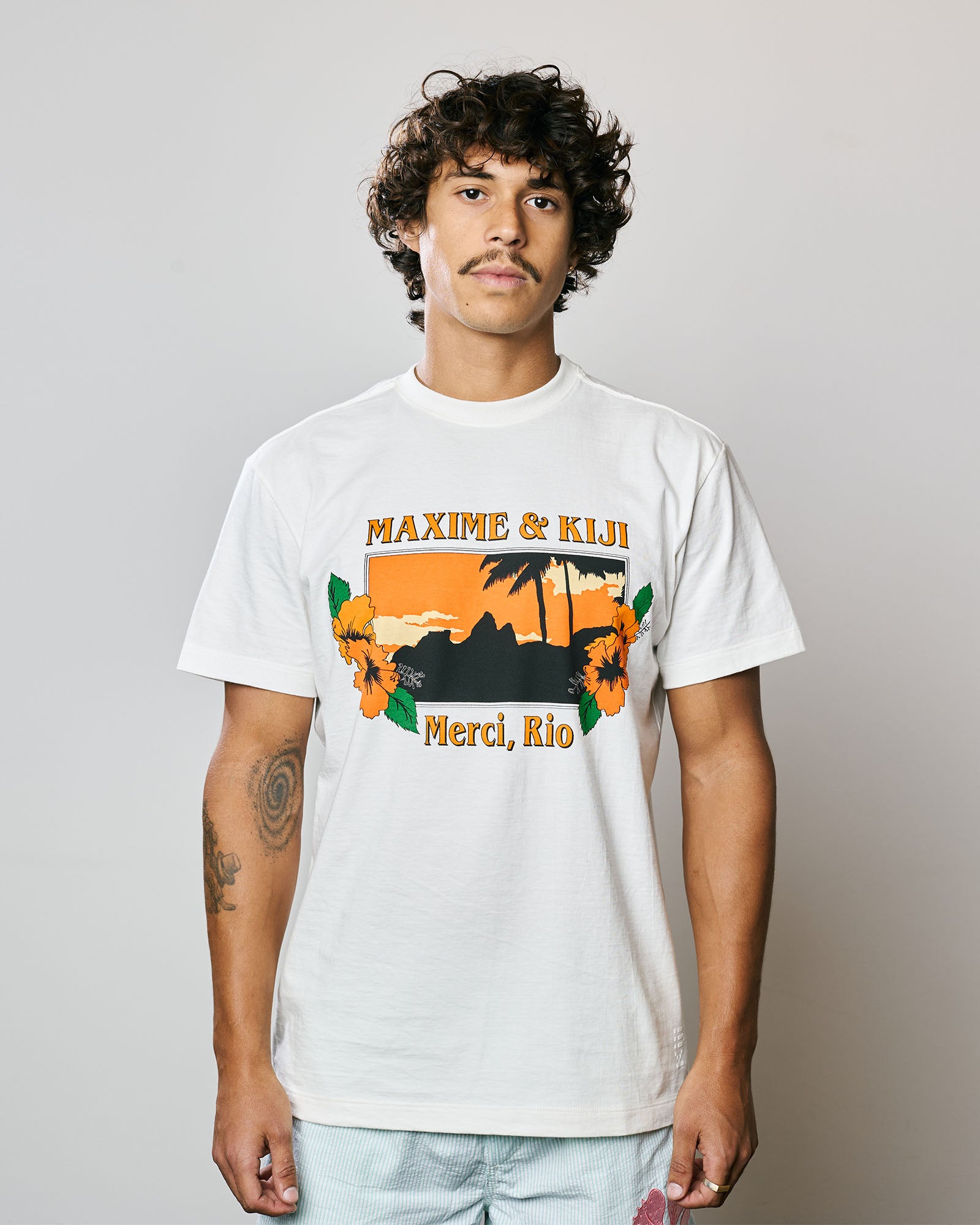 Modelo vestindo a T-Shirt Classic Kiji x Maxime Merci Rio na cor Off White, com estampa tropical.