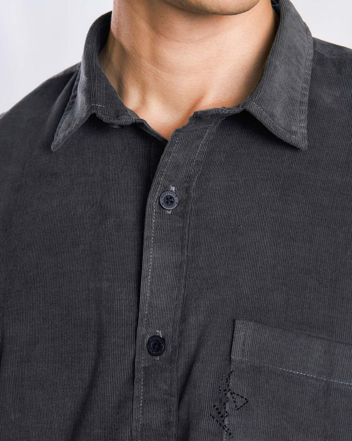 Detalhe do modelo vestindo Camisa de botão Kiji de frente, com bolso frontal no lado esquerdo, com logo bordado, na cor preto.