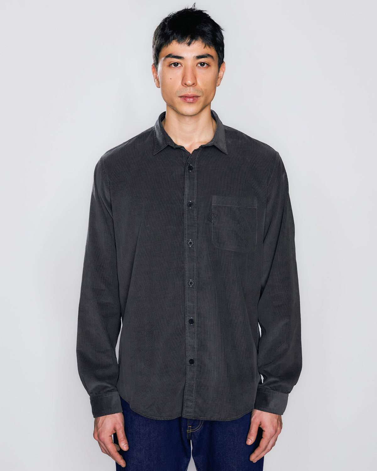 Modelo vestindo Camisa de botão Kiji de frente, com bolso frontal no lado esquerdo, com logo bordado, na cor preto.