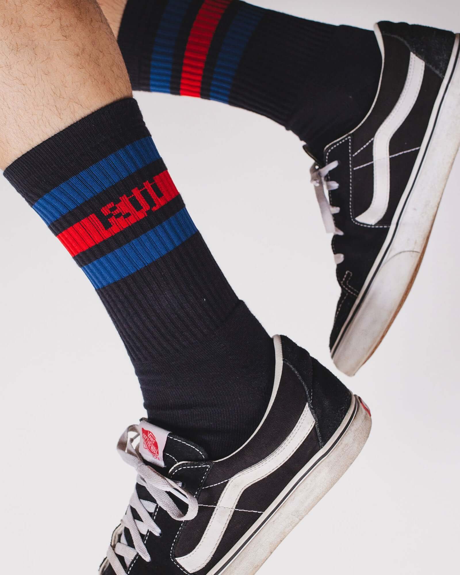 Foto de detalhe, zoom no pé do modelo vestindo a meia Kiji Stripes SK8 de algodão e um tênis preto.