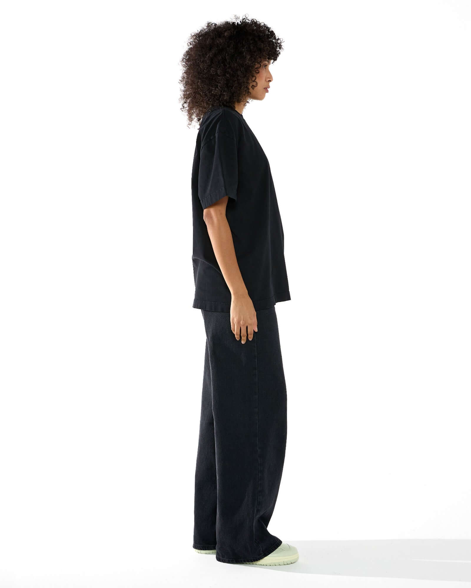 Modelo feminina vestindo a camiseta oversized preta Kiji, virada para o lado direito.