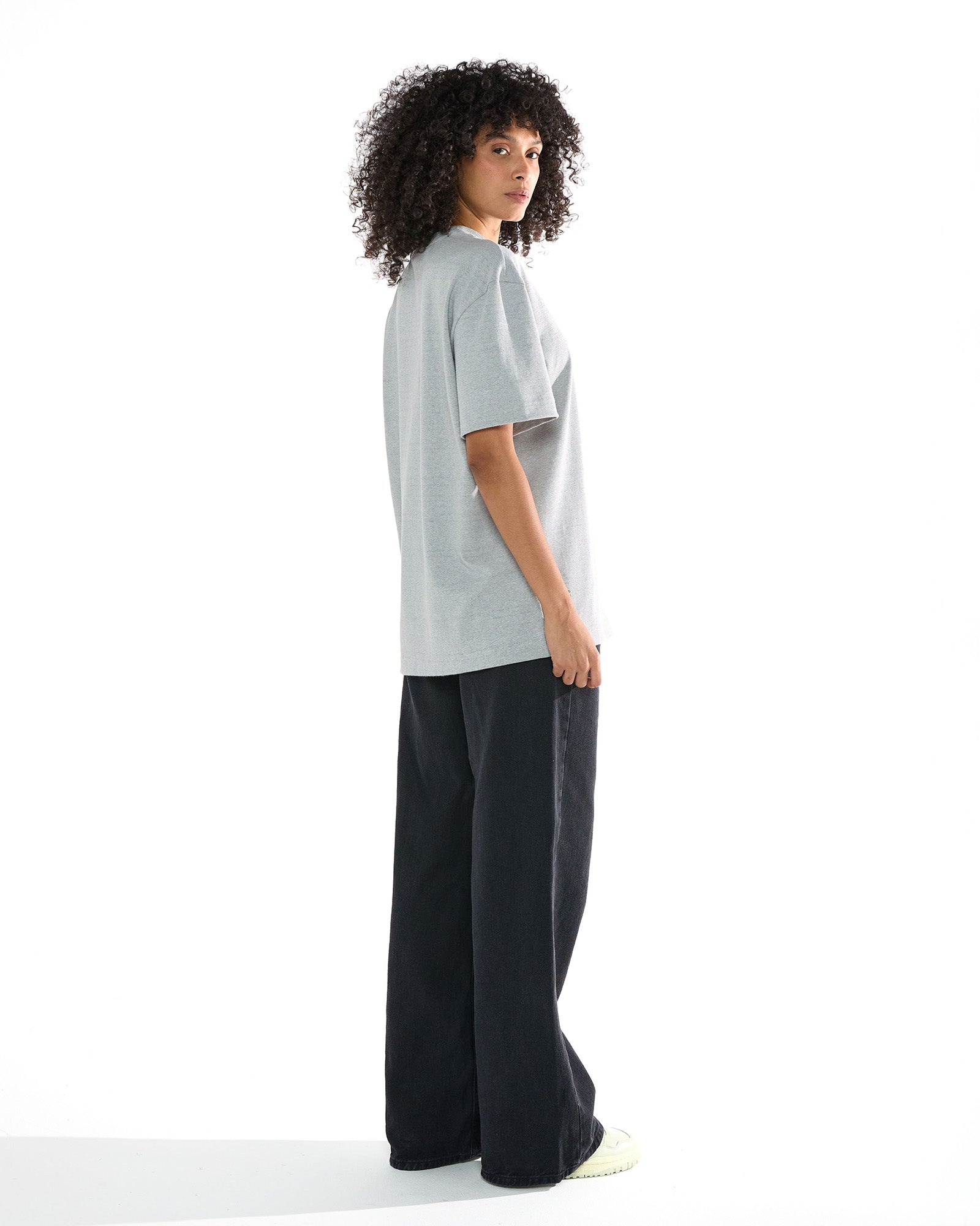 Modelo feminina vestindo a camiseta oversized cinza mescla Kiji, virada para o lado direito.