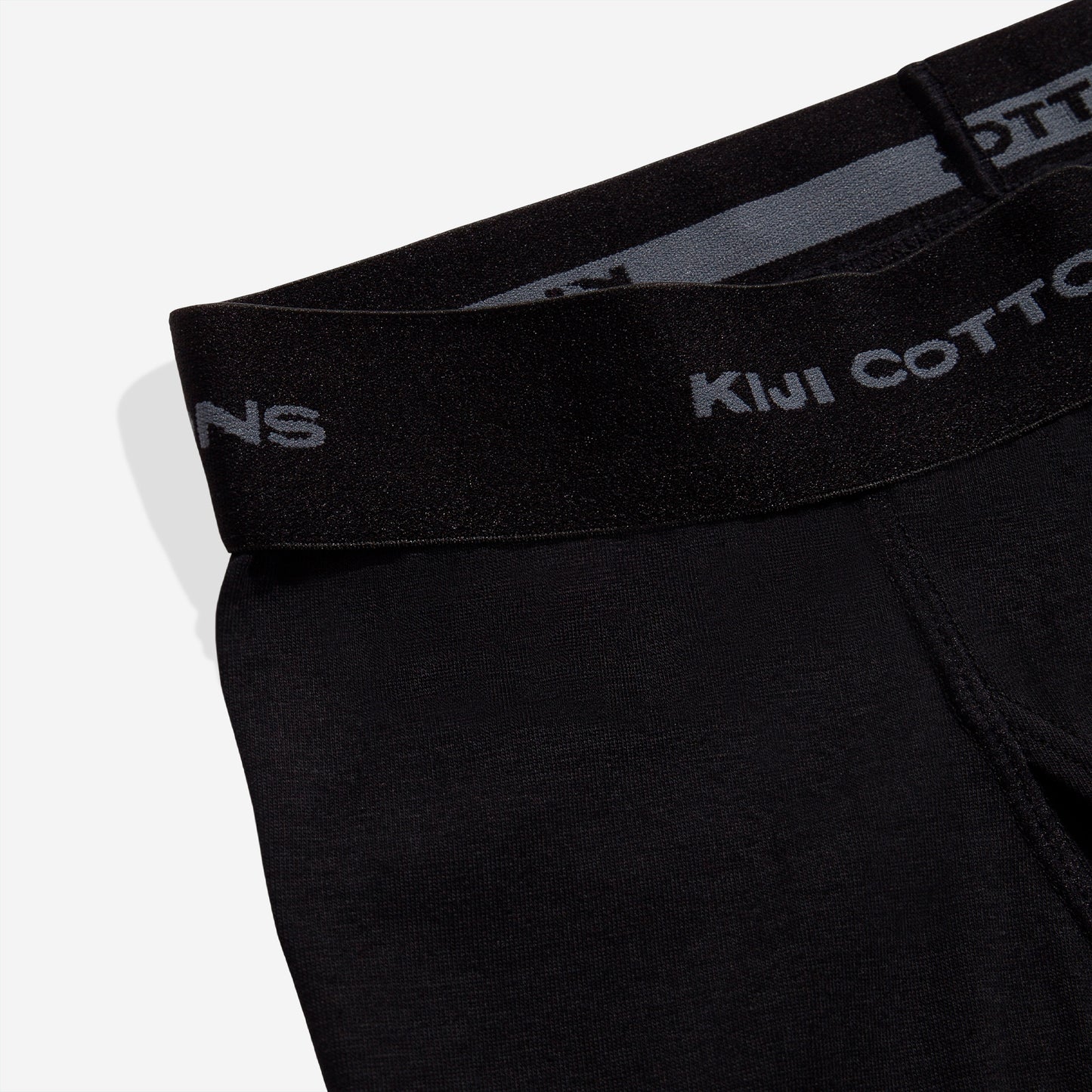 Foto de detalhe com zoom no elástico da cueca kiji boxer preta, onde está escrito kiji cottons.