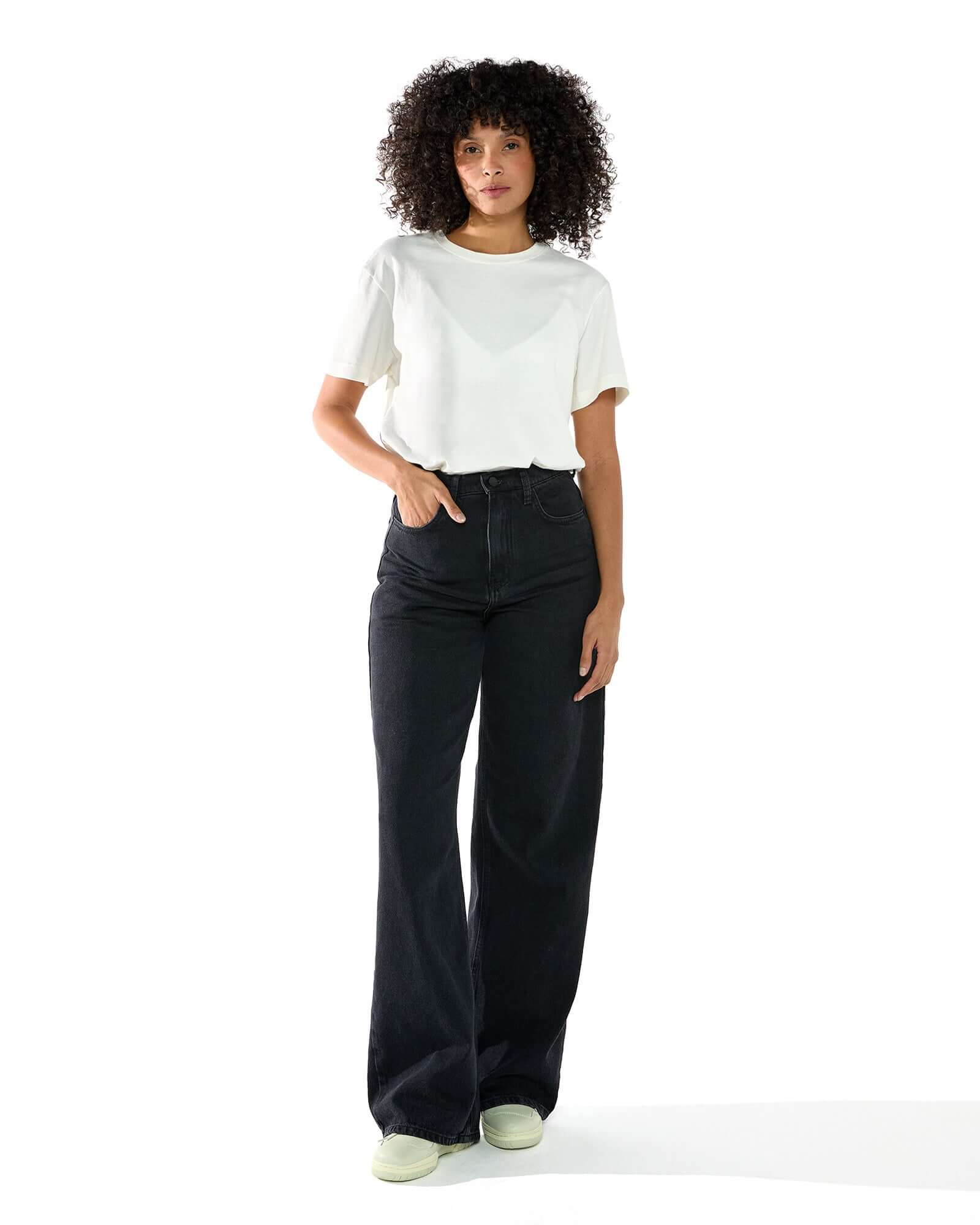 Foto de corpo inteiro da Modelo feminina vestindo a t-shirt classic Kiji de algodão na cor off white e calça jeans preta.