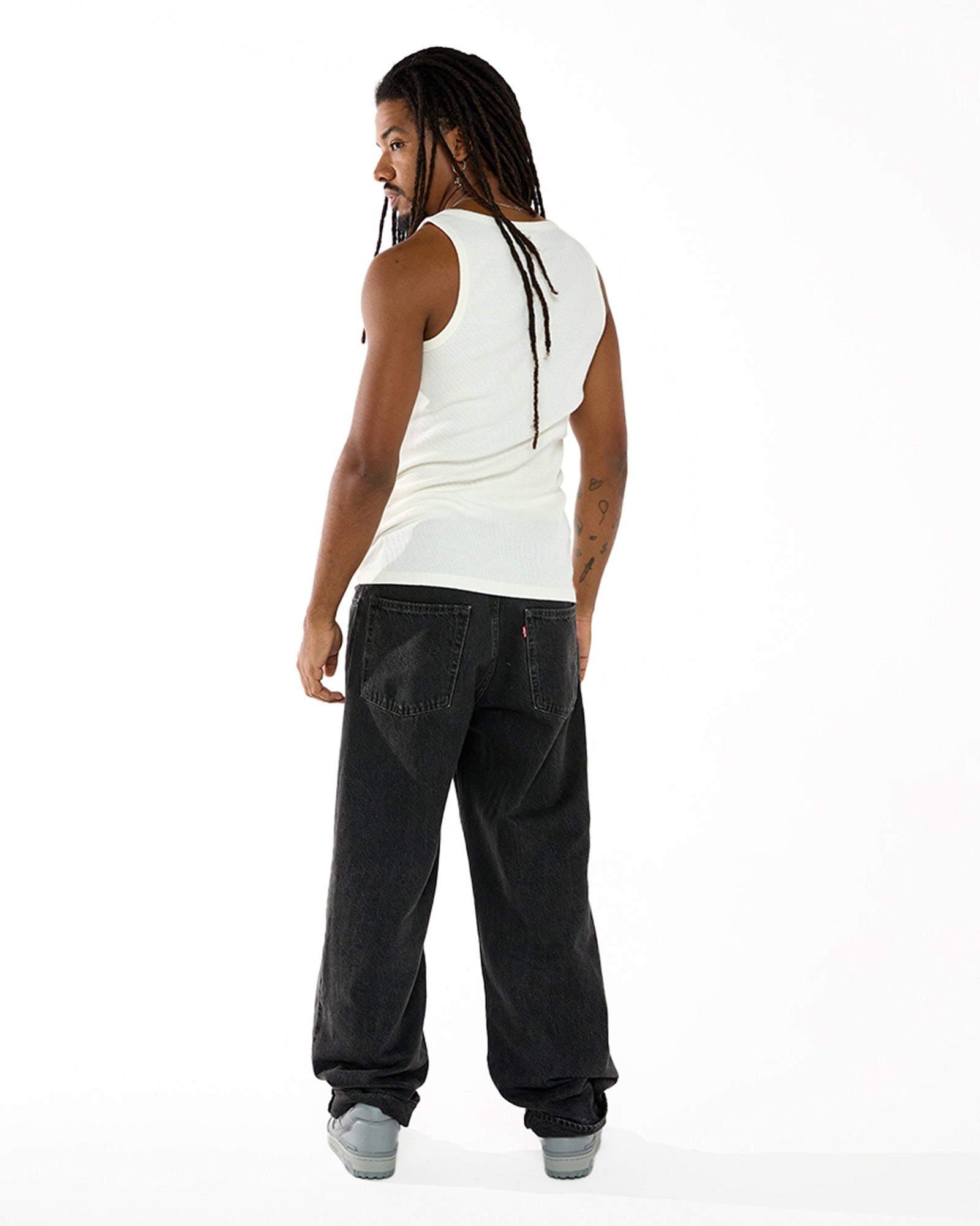 Modelo Negro, de Dreads e calça preta, posando de costas e vestindo a regata canelada Tank-Top Kiji na cor Branca