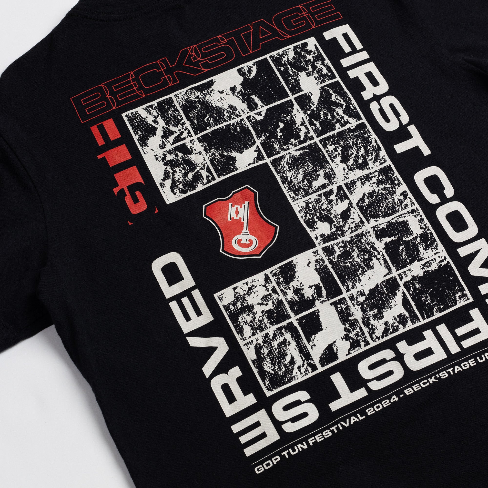 Foto de detalhe da T-Shirt Classic Kiji Beck'stage Preta, a estampa da costas consiste em vários quadrados brancos com imagens de um relevo do terreno, no meio há o um brasão vermelho com uma chave dentro, e ao redor desses quadrados está escrita os seguintes dizeres: "GTF" "Beck'stage""First come first served"