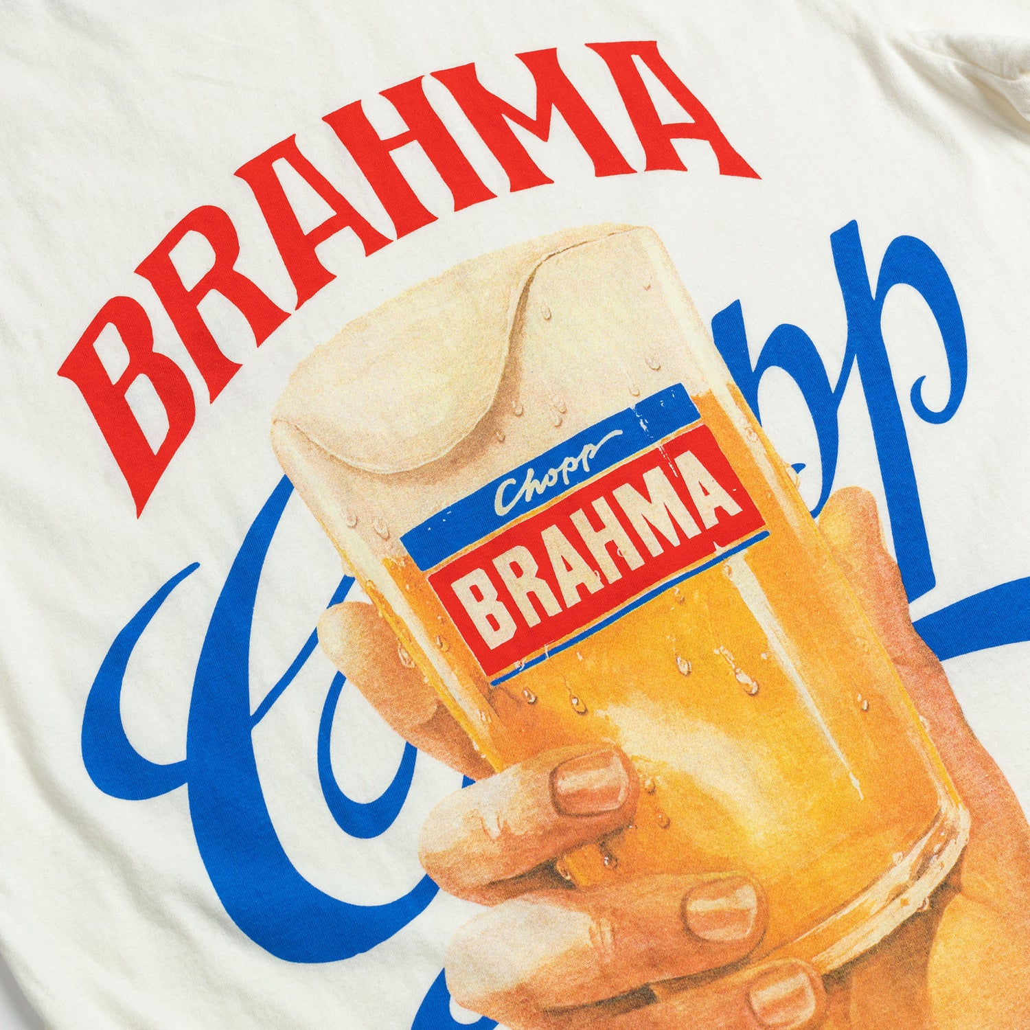 Foto de Detalhe da T-Shirt Classic off-white Kiji x Brahma Chopp, a estampa consiste no logo da brahma com suas cores tradicionais (vermelho e azul) e o desenho de uma mão segurando um copo de cerveja com o colarinho transbordando.