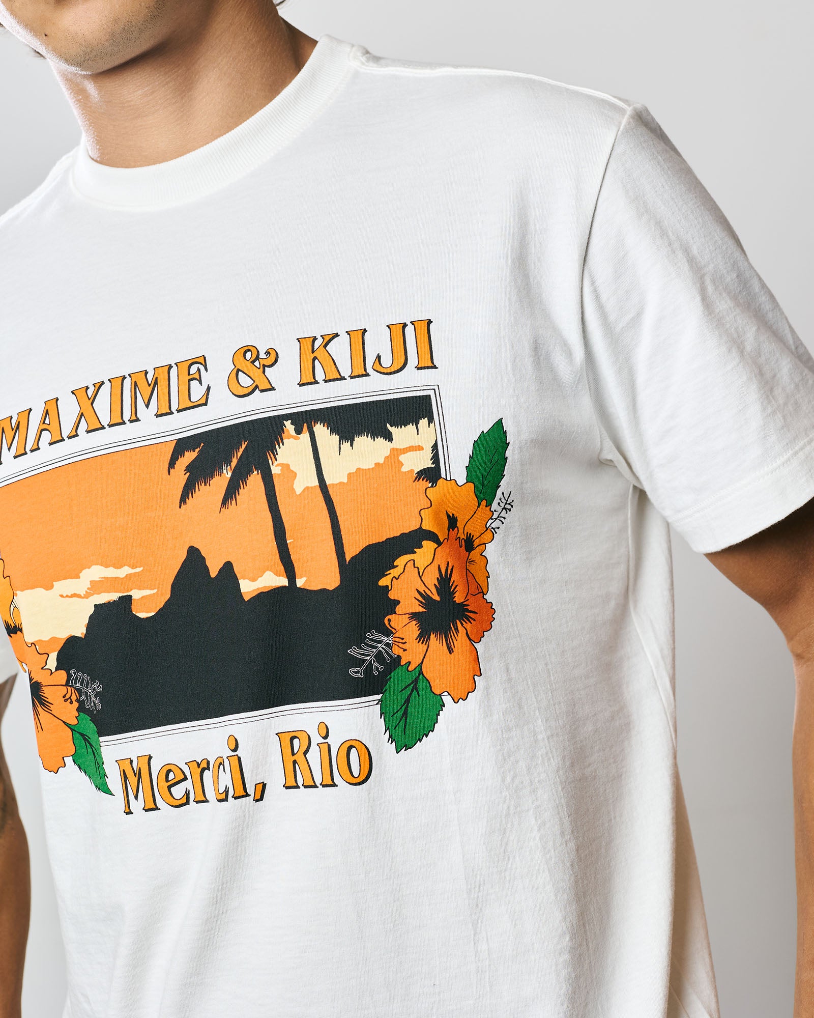 T-Shirt Classic Kiji x Maxime Merci Rio em Off White, com estampa floral vibrante e pôr do sol, em modelagem unissex.