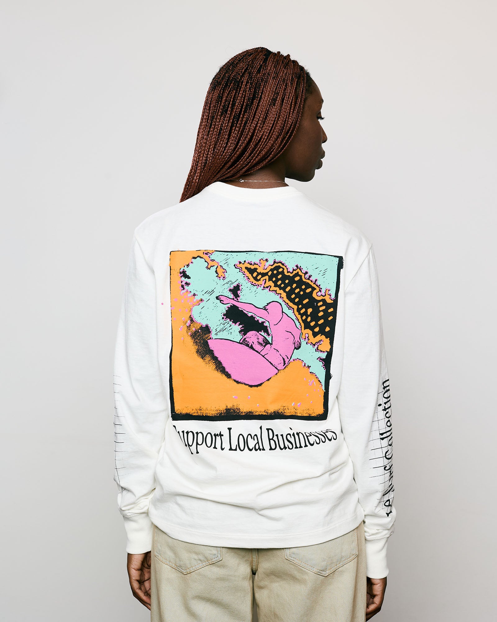 Vista traseira de modelo usando camiseta de manga longa com arte colorida e a frase “Support Local Businesses”.