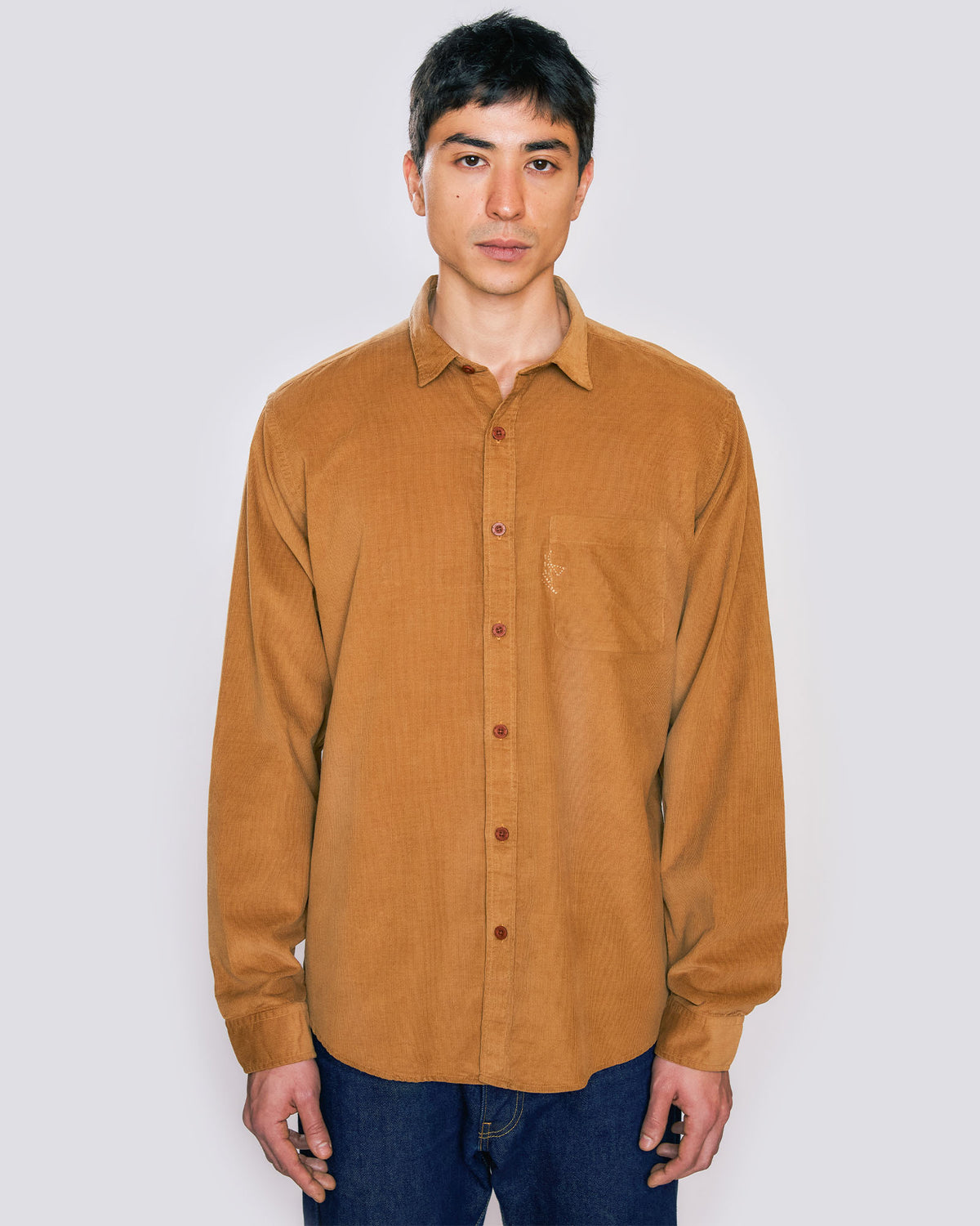 Modelo vestindo Camisa de botão Kiji de frente, com bolso frontal no lado esquerdo, com logo bordado, na cor caramelo.
